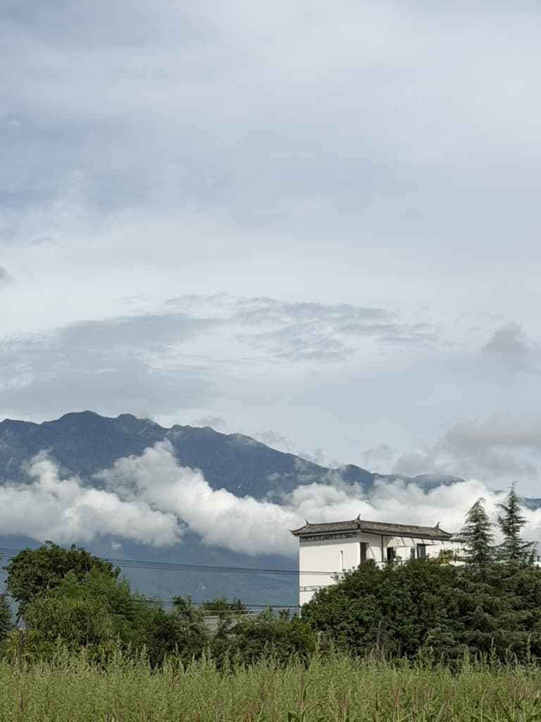 Clouds drifting across the lower slopes of a mountain range, above a white house with a tiled roof